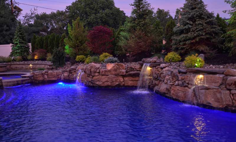 Swimming pool at night, surrounded by a wall of lighted boulders and two waterfalls