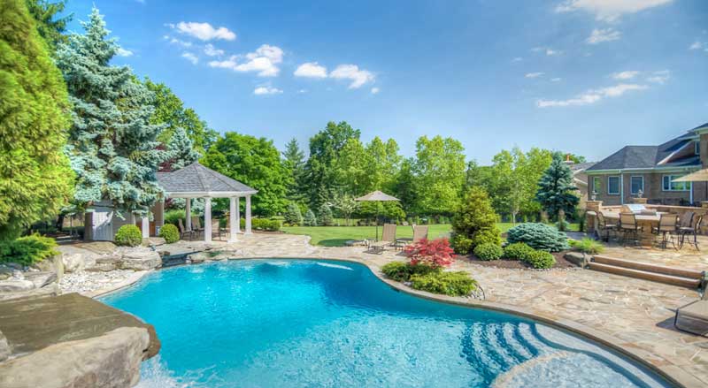 A backyard with a large pool, expansive patio, gazebo, and dining area