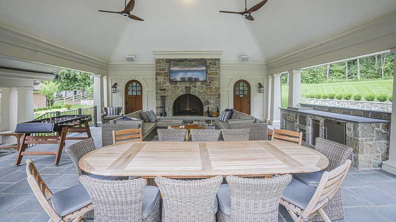 Outdoor living space in a pavilion with stone fireplace, outdoor kitchen, dining and entertainment area