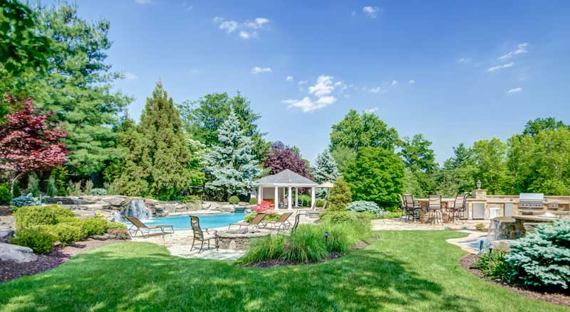 Back yard with a stunning landscape design with pool, waterfall, gazebo, patios, and beautiful plantings