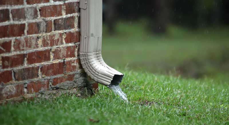 A short downspout draining rainwater next to a foundation.