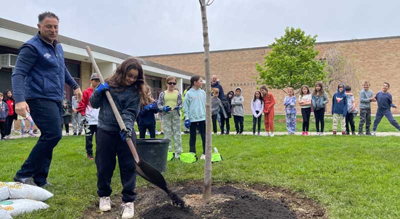 Student shovels dirt around a newly planted tree