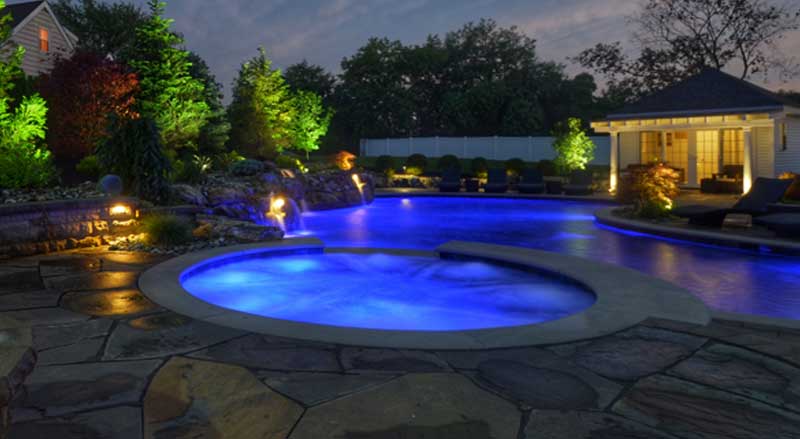 Outdoor lighting enhances a pool with a round jacuzzi at night