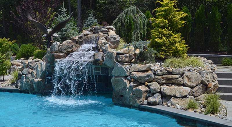 A pool waterfall made of small boulders and other natural stone.