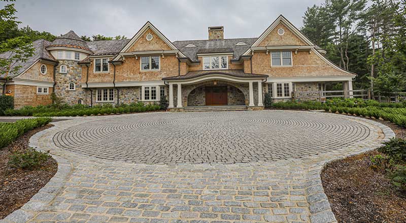 A circular stone driveway with a combination of hardscaping materials and techniques in front of a beautiful home