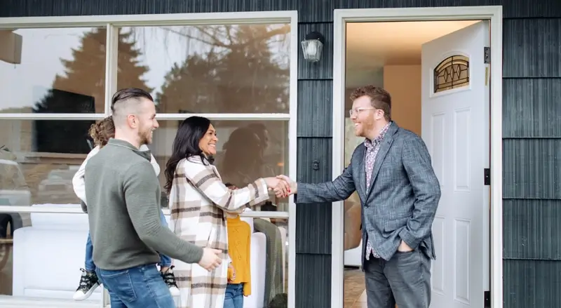 A man, woman, and child being greeted at the front door of a house