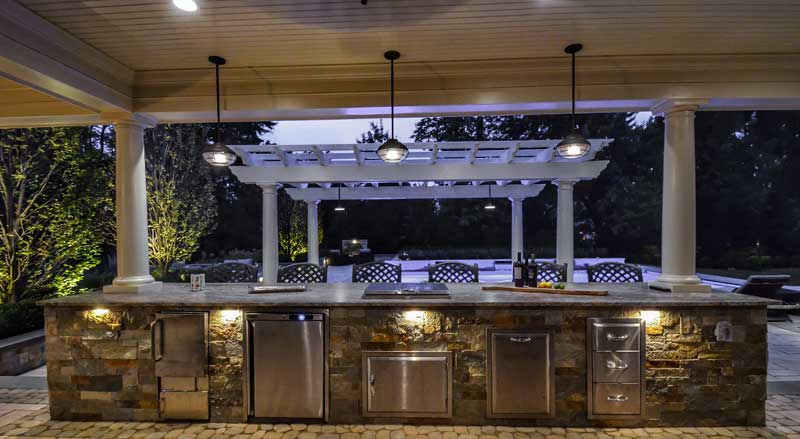 An outdoor kitchen in front of a pool lit at night