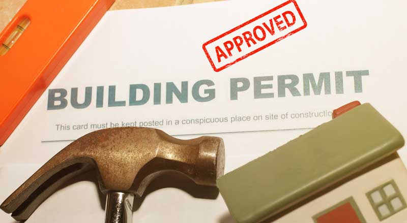 A building permit placed next to a hammer, representing the tools and documentation necessary for landscaping or construction projects