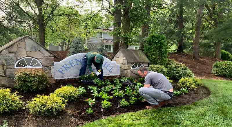 Landscape professionals at Sponzilli Landscape Group are planting new flowers at the entrance of an HOA neighborhood