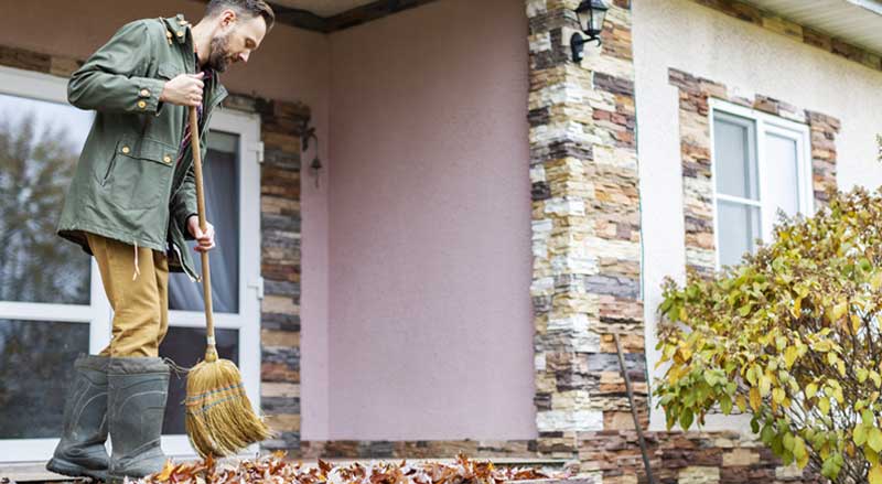 A man sweeping leaves off his front porch