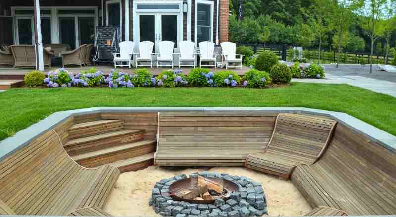 A uniquely built large fire pit with plenty of seating and a large home in the background