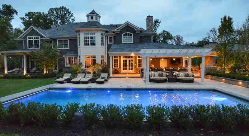 A tranquil backyard that features a swimming pool, a pergola, with plenty of seating for guests