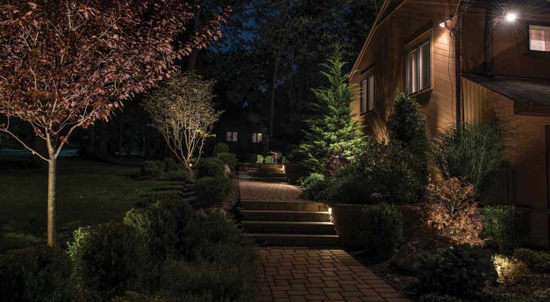 Front walkway of a home at night with planted gardens and landscape lighting