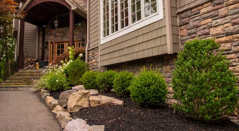 Grand entryway with a paved driveway, layered landscaping, and a mix of perennials and evergreens.