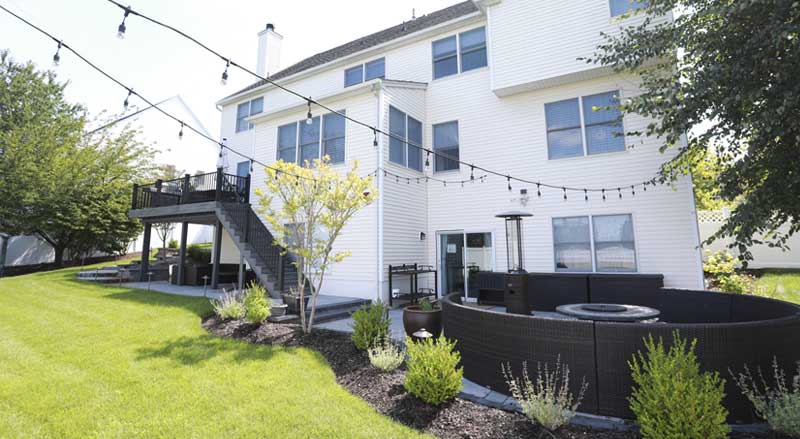 Multi-level backyard with upper deck, string lighting, and a cozy circular patio featuring a fire pit and outdoor seating