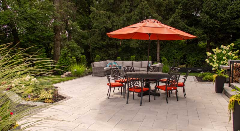 Stylish stone patio with black wrought-iron dining set, vibrant orange umbrella, and a comfortable lounge area