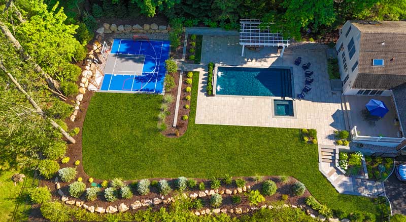 Aerial view of a refreshed residential landscape with a pool, spa, sports court, and newly planted garden beds