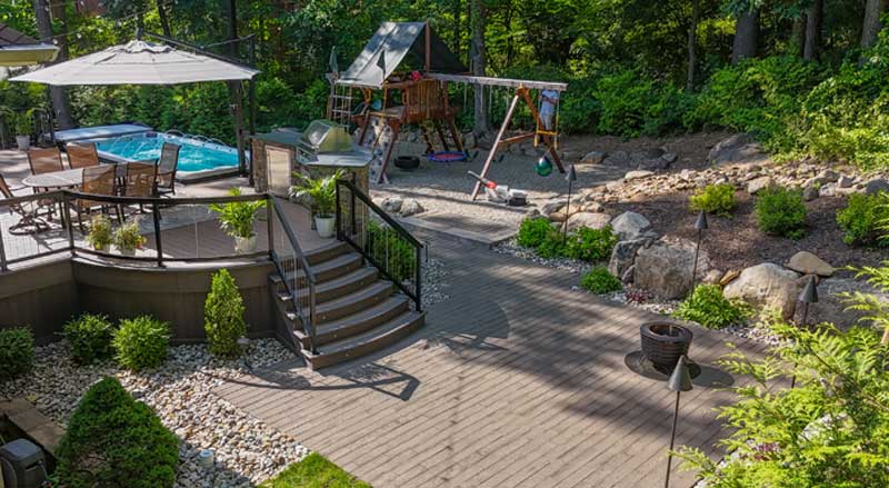 Backyard makeover including a children’s playset, pool, multi-level patio, and decorative landscaping rocks