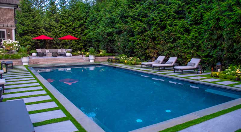 Luxurious pool with clean hardscape lines, lounge chairs, and privacy provided by mature privacy trees