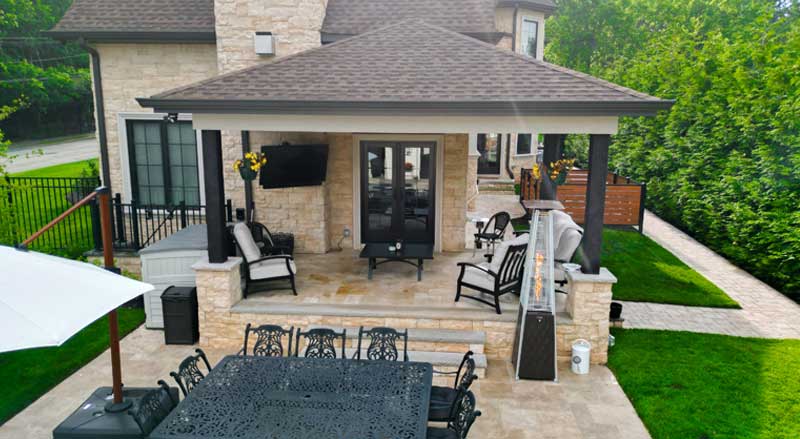 Elegant covered patio with black pillars, cozy lounge seating, mounted outdoor TV, and wrought iron dining furniture