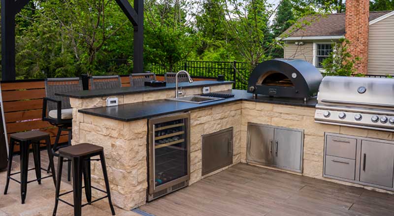 Stylish stone outdoor kitchen featuring a built-in grill, pizza oven, and bar seating.