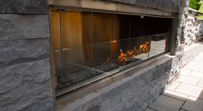Sleek built-in linear fireplace set in gray stone with glass panels