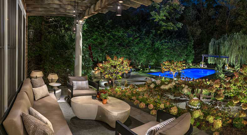 Serene outdoor lounge with modern seating, soft overhead lighting, and illuminated garden beds