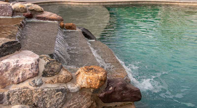 Luxury pool with built-in stone water feature with natural rock textures