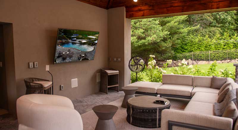 Cozy covered outdoor lounge area with neutral-toned sectional seating and smart TV