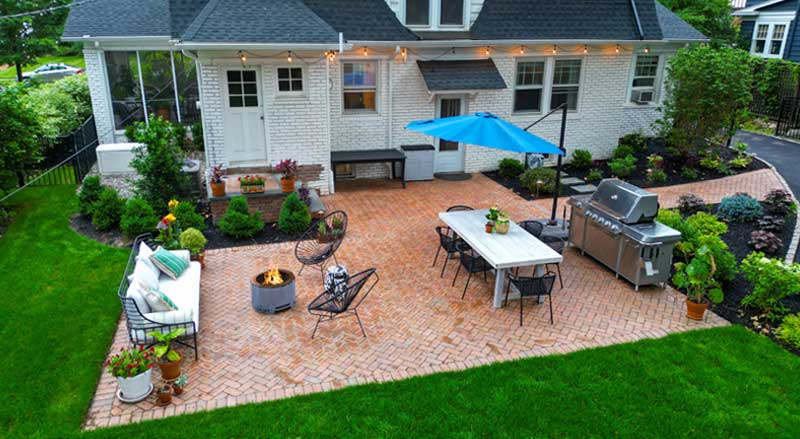Backyard patio with herringbone brick flooring, string lights, a dining setup