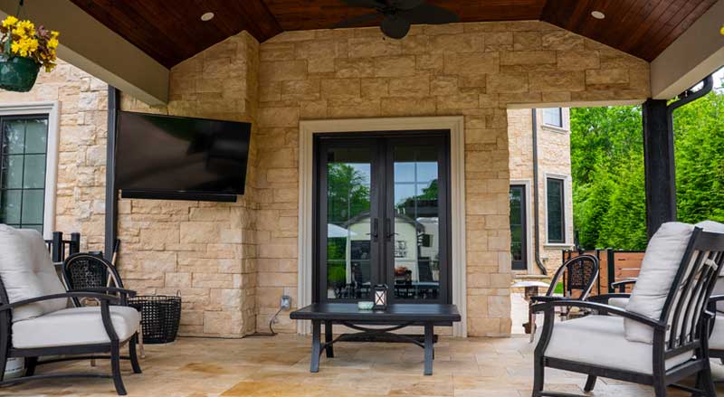 Covered pavilion with stone walls, outdoor TV, and cushioned chairs—blending durability and style in backyard living spaces