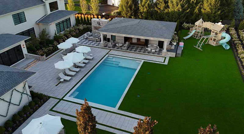 Spacious New Jersey backyard featuring a modern pool, lounge chairs, and a large playset, showcasing a manicured fall-ready lawn