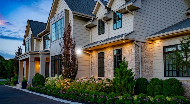 Front yard landscape design with manicured shrubs, stone façade, and pathway lighting enhancing curb appeal of a luxury NJ home