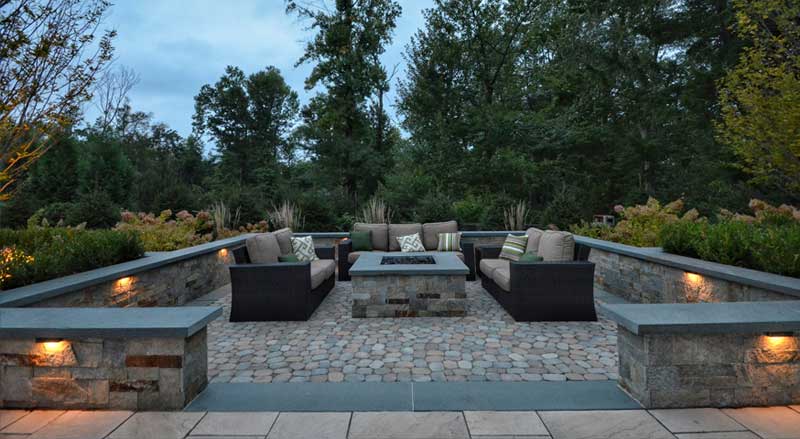 Elegant backyard patio with built-in stone fire pit, accent lighting, and modern seating