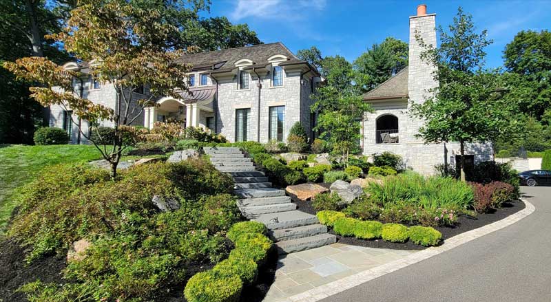 Professional landscape with tiered stone steps, ornamental trees, and foundation plantings that elevate curb appeal