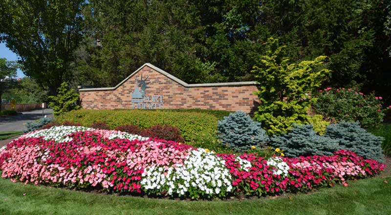 HOA entrance sign framed by seasonal flowers and evergreen shrubs