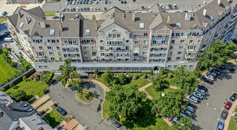 Aerial view of an HOA condo community with landscaped entry, mature trees, and maintained grounds
