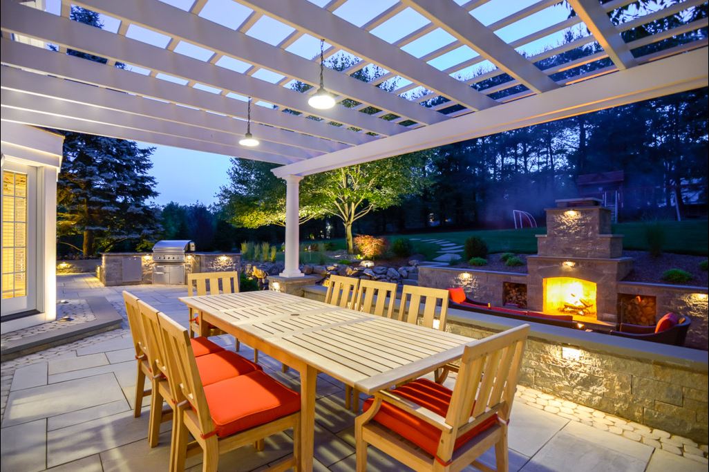 Stone outdoor kitchen and fireplace with seating and landscape lighting at dusk