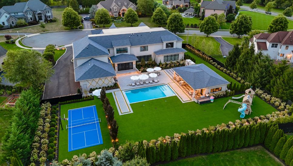 Aerial view of a complete estate pool landscape with patio, pavilion, lawn, sport court, and privacy plantings