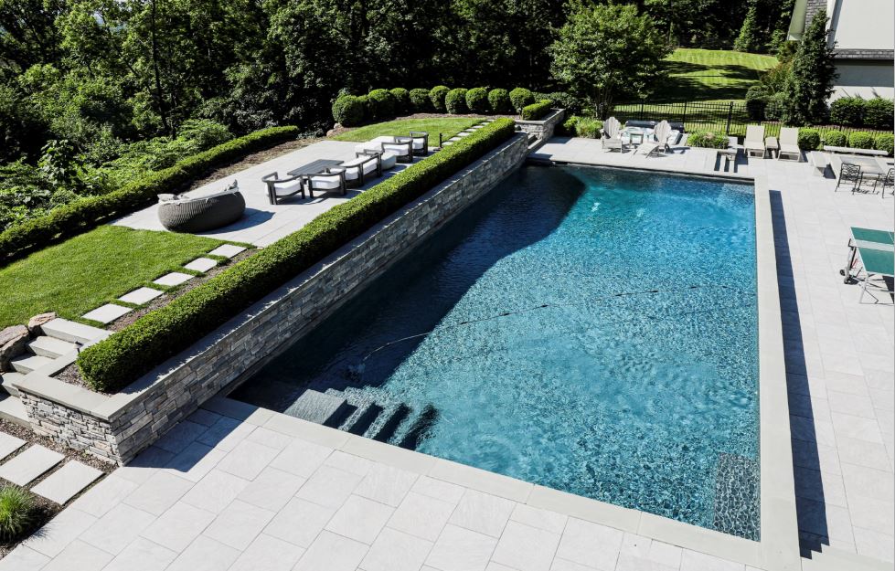 Modern swimming pool with stone retaining wall, wide patio, steps, and formal landscape plantings