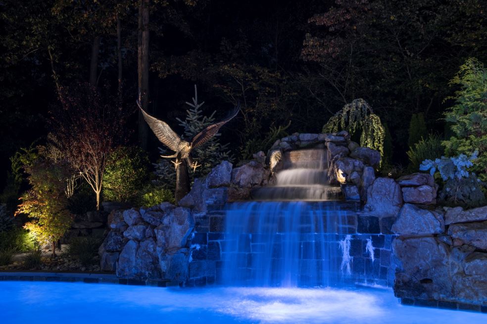 Illuminated pool waterfall with natural stone, specimen plantings, and professional landscape lighting